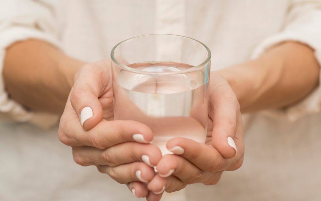 A closeup on two hands holding a glass of water.