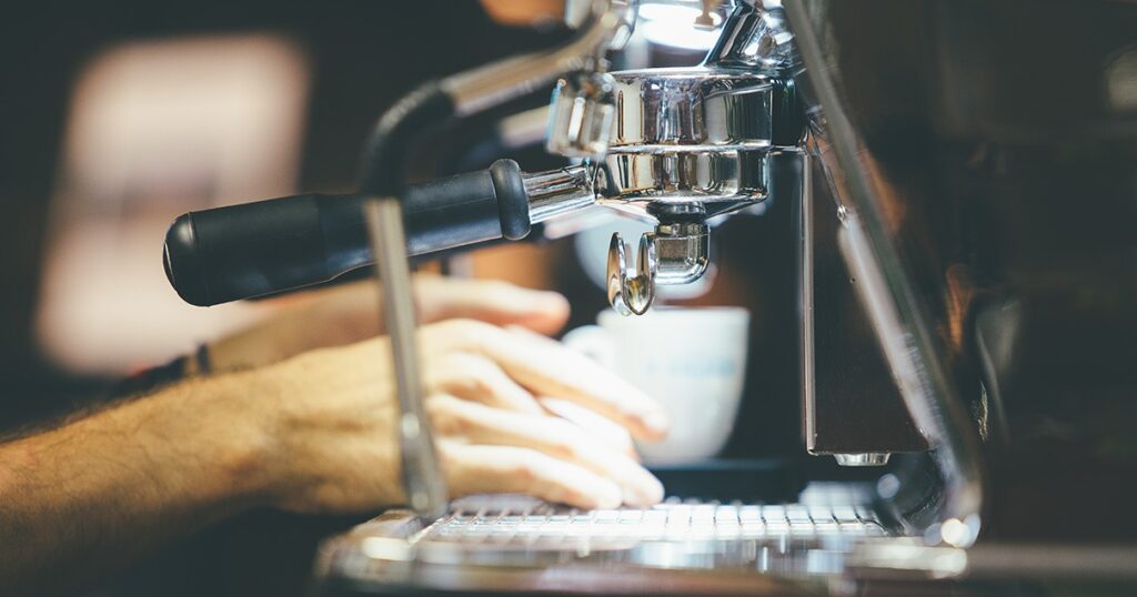 A barista putting a coffee cup under a coffee machine's portafilter.